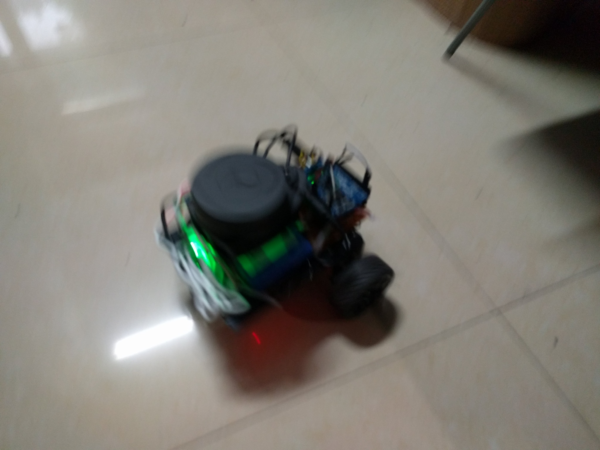A small homemade robot car moving across a tiled floor with green lights on.