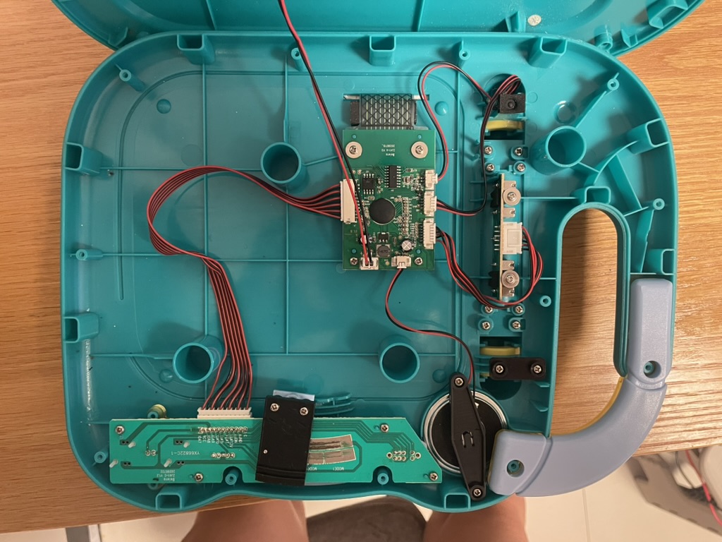 Opened teal electronic learning book showing the circuit board, wiring, speaker, and battery contacts.